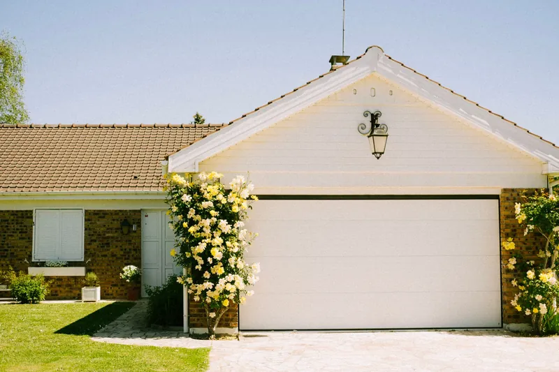Maison individuelle avec porte de garage sectionnelle blanche encadrée de rosiers grimpants jaunes
